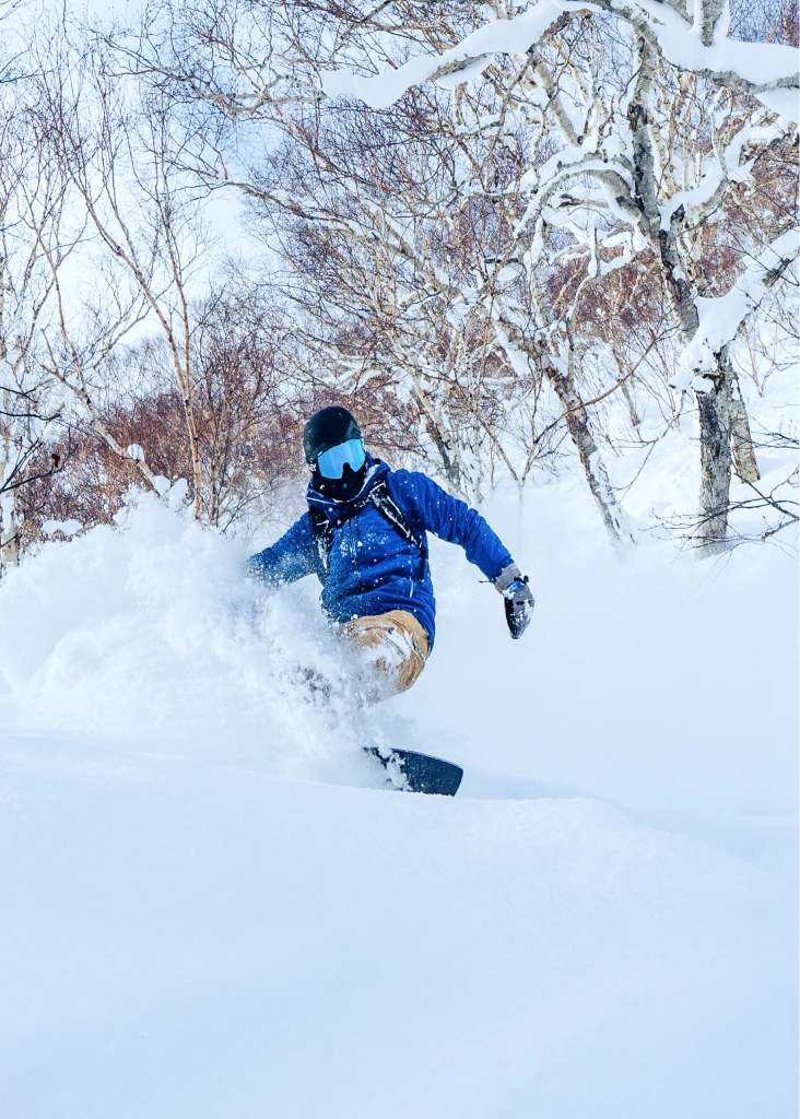 Snowboarder riding through deep powder in a snowy forest